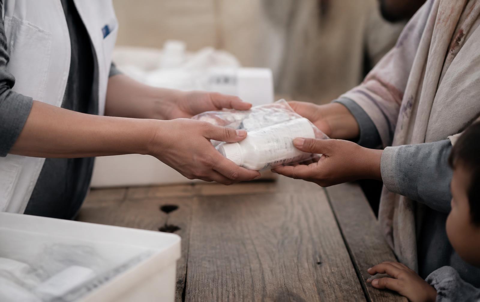 A volunteer handing a parcel of medical supplies to a family across a wooden table
